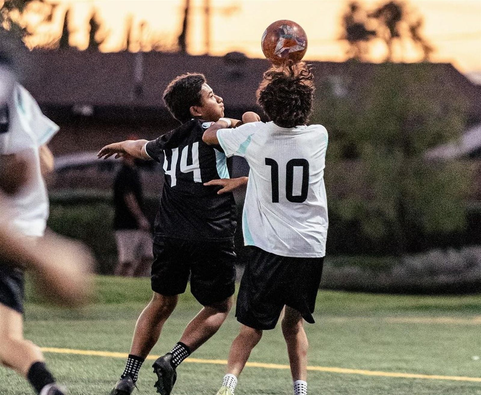 Players jumping for a header at sunset