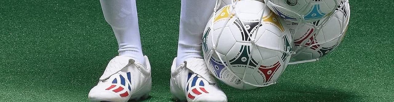 Footballs in a net beside a player's boots on the pitch